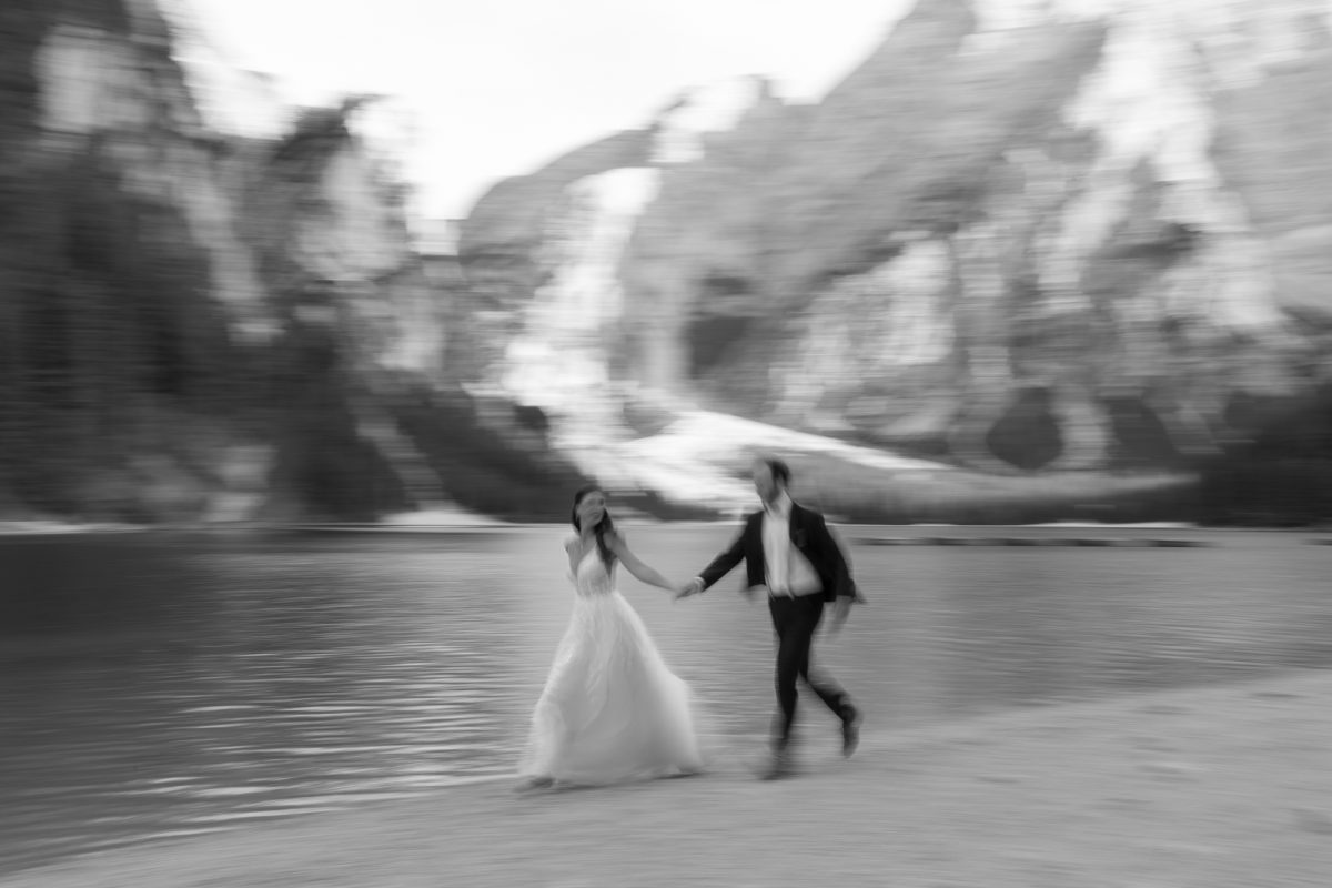 Laura und Tommy laufen beim After Wedding Shooting Hand in Hand am Ufer des Pragser Wildsees (Schwarz-Weiß-Aufnahme)