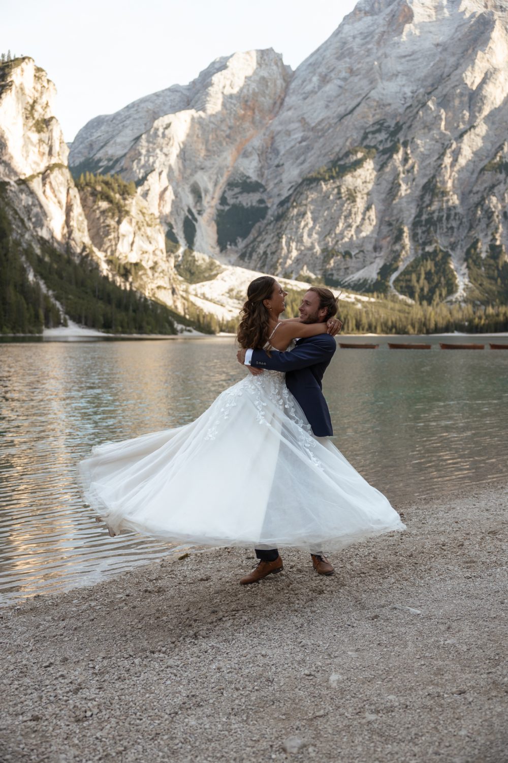 Tommy hebt Laura hoch, ihr Brautkleid wirbelt am Ufer des Pragser Wildsees
