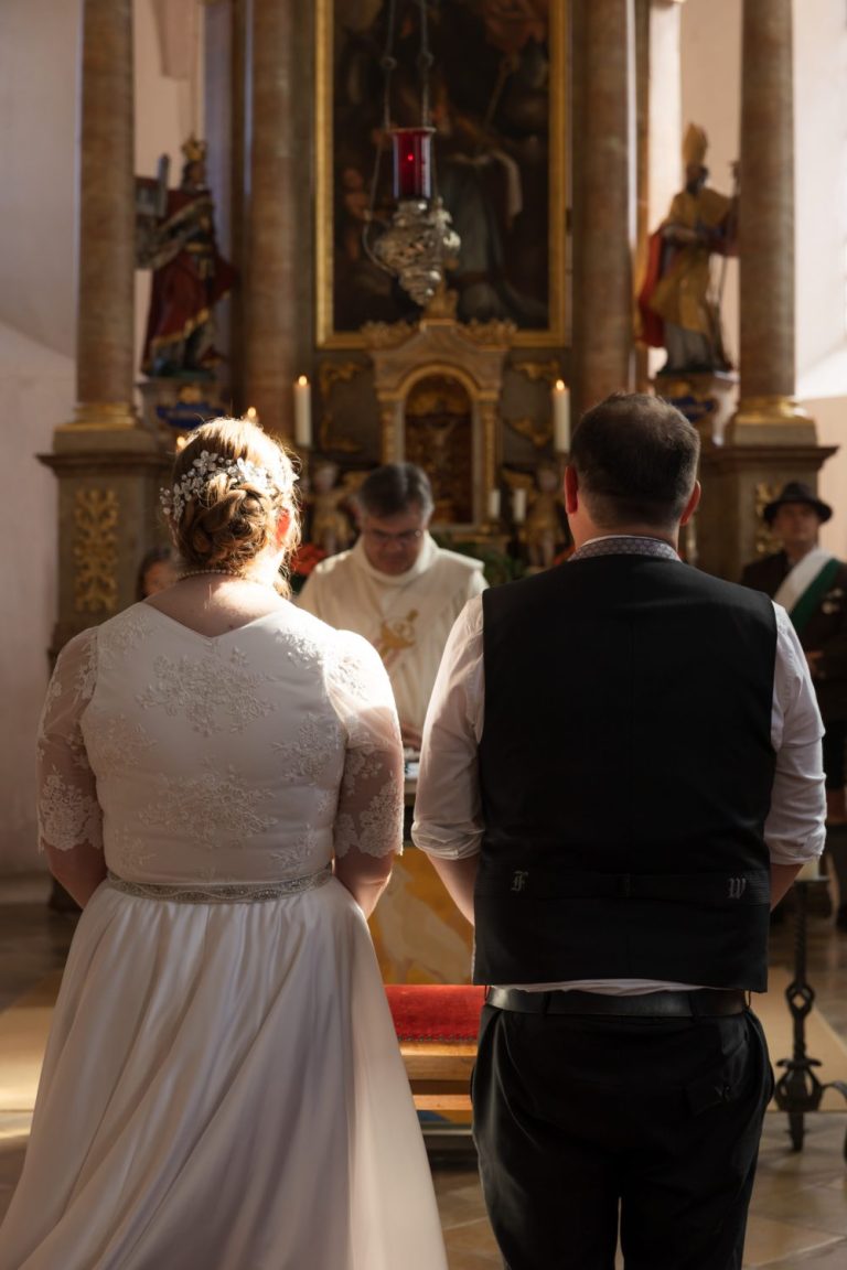 Brautpaar von hinten vor dem Altar einer Kirche, dahinter der Pfarrer