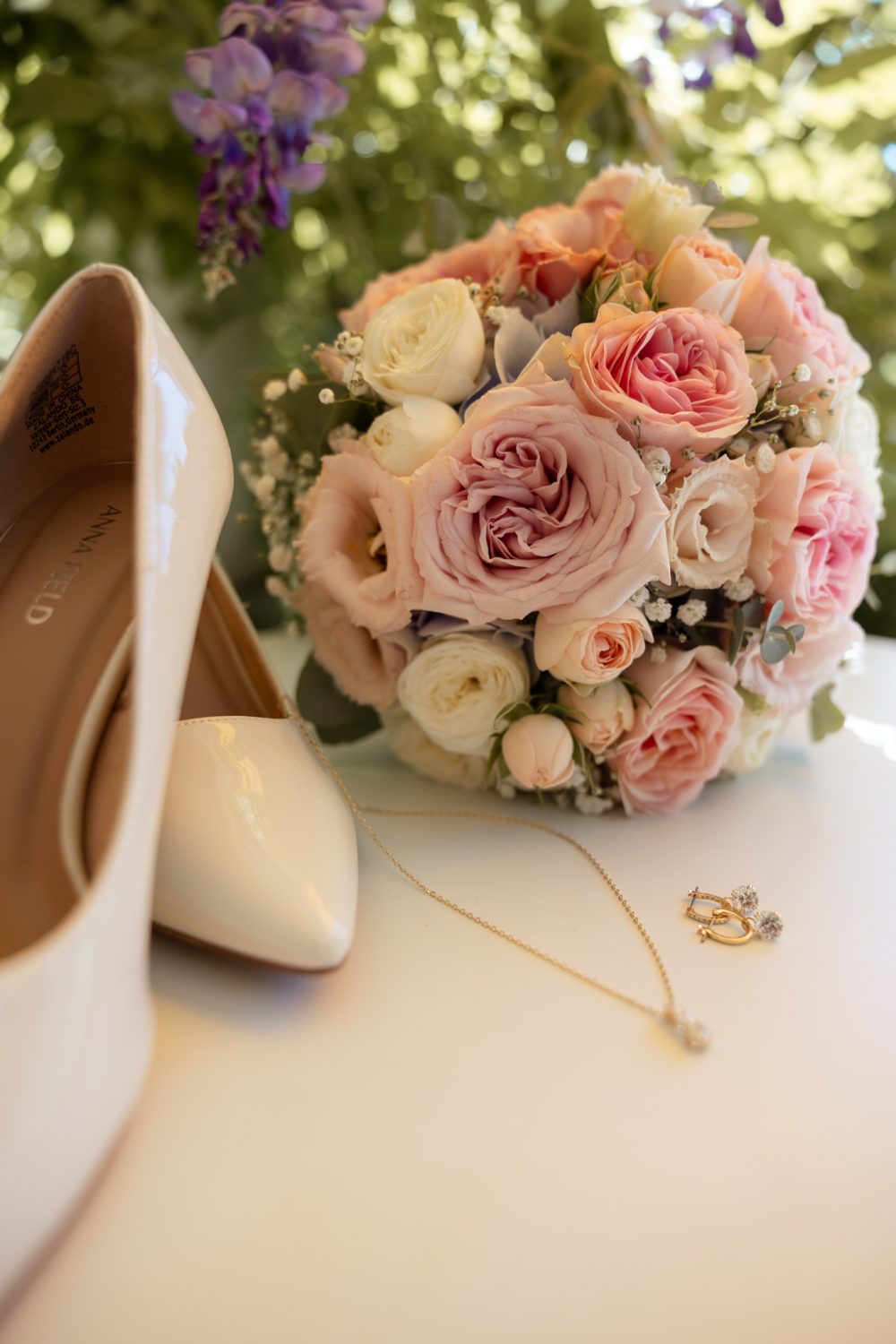 Brautstrauß in Rosa und Weiß neben Brautschuhen und einer Kette auf einem Tisch