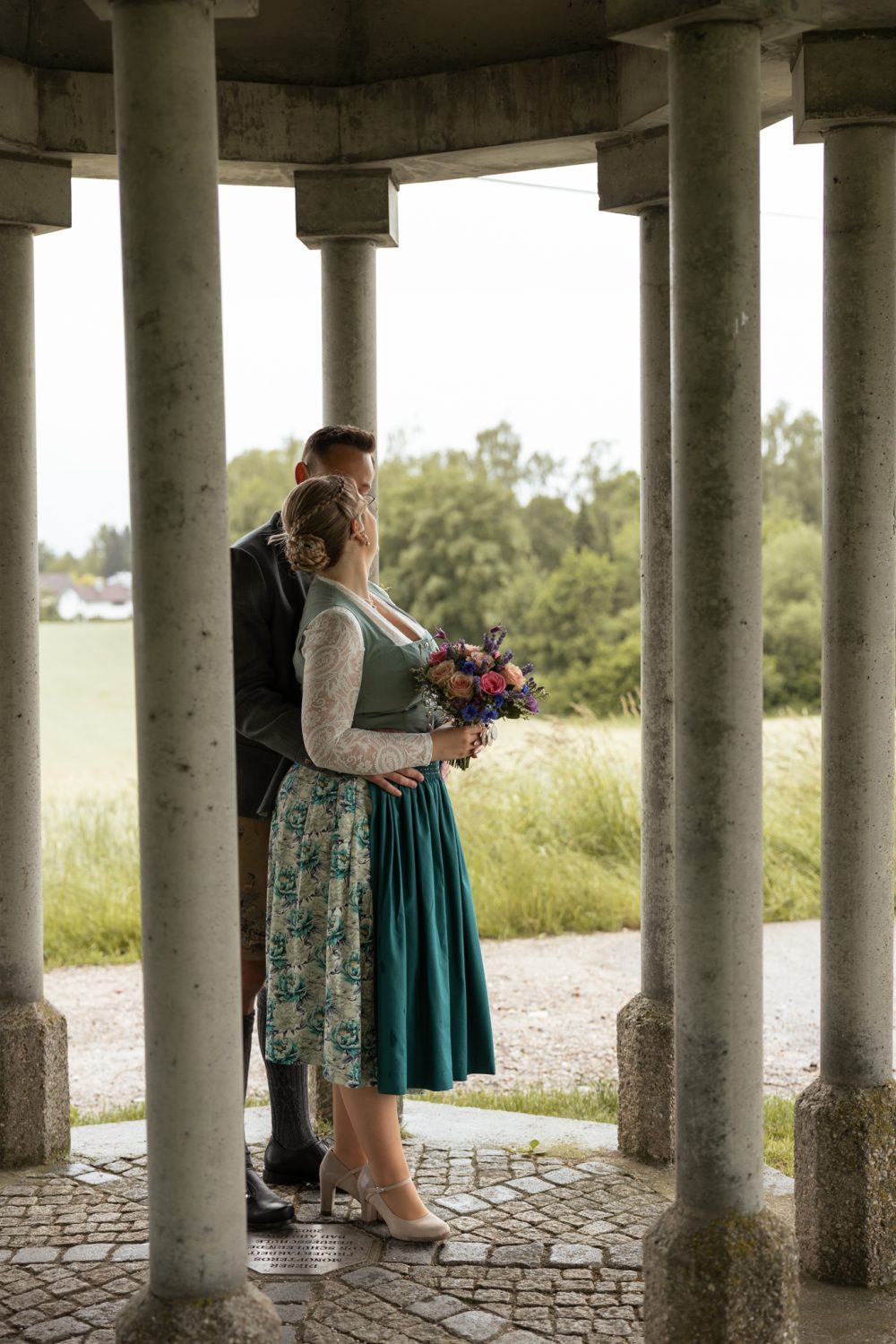 Paar in einem Pavillon, sie im geblümten Kleid mit Brautstrauß