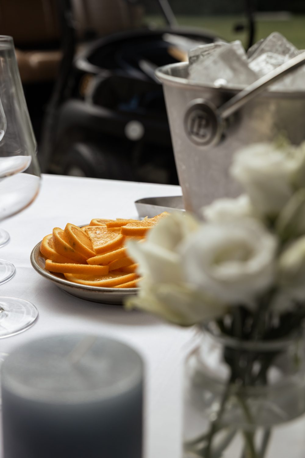 Tisch mit Orangenscheiben, weißen Blumen, Sektkühler und grauen Kerzen im Vordergrund