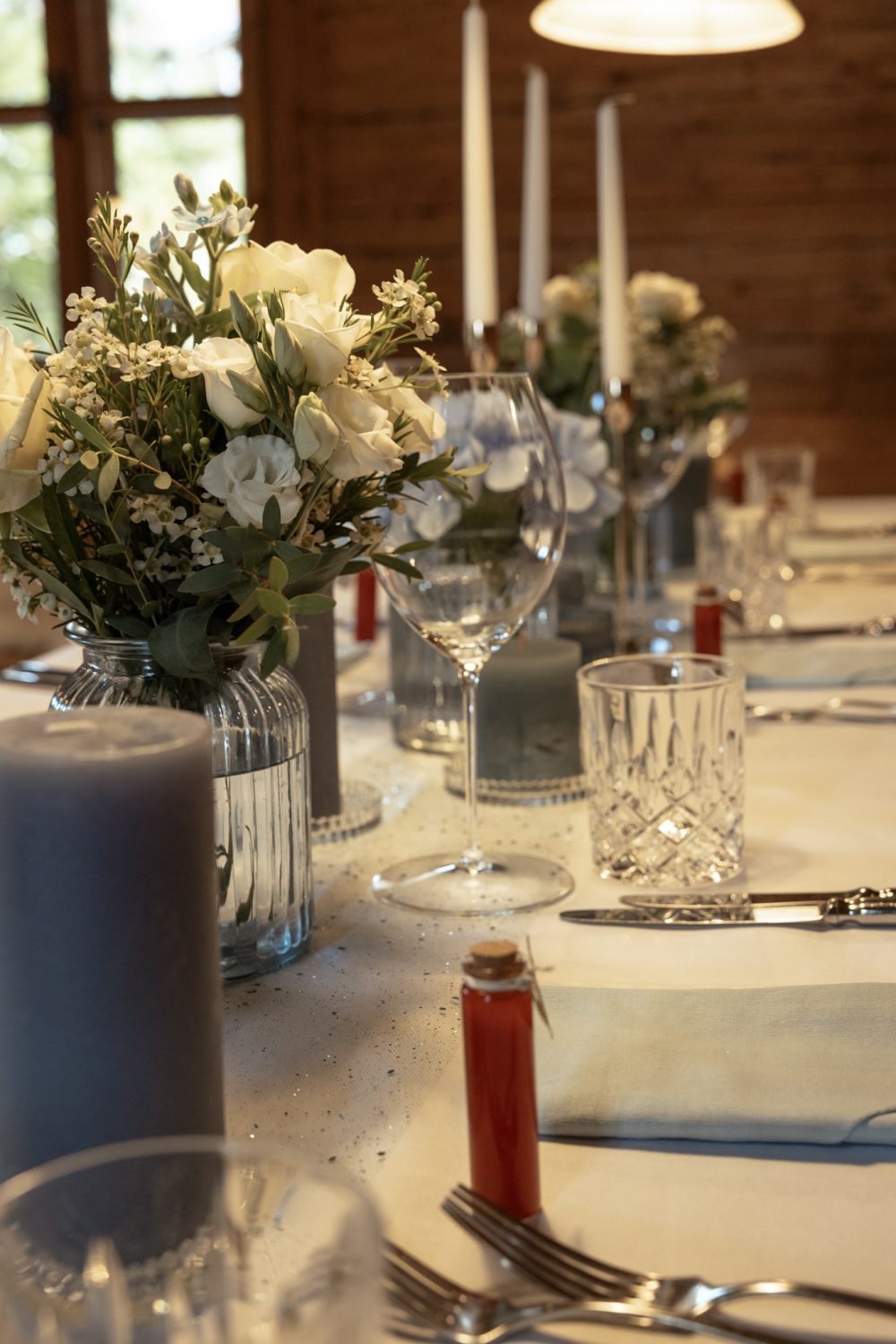 Festlich gedeckte Tafel mit Blumen, Kerzen und Gläsern in einer holzverkleideten Stube