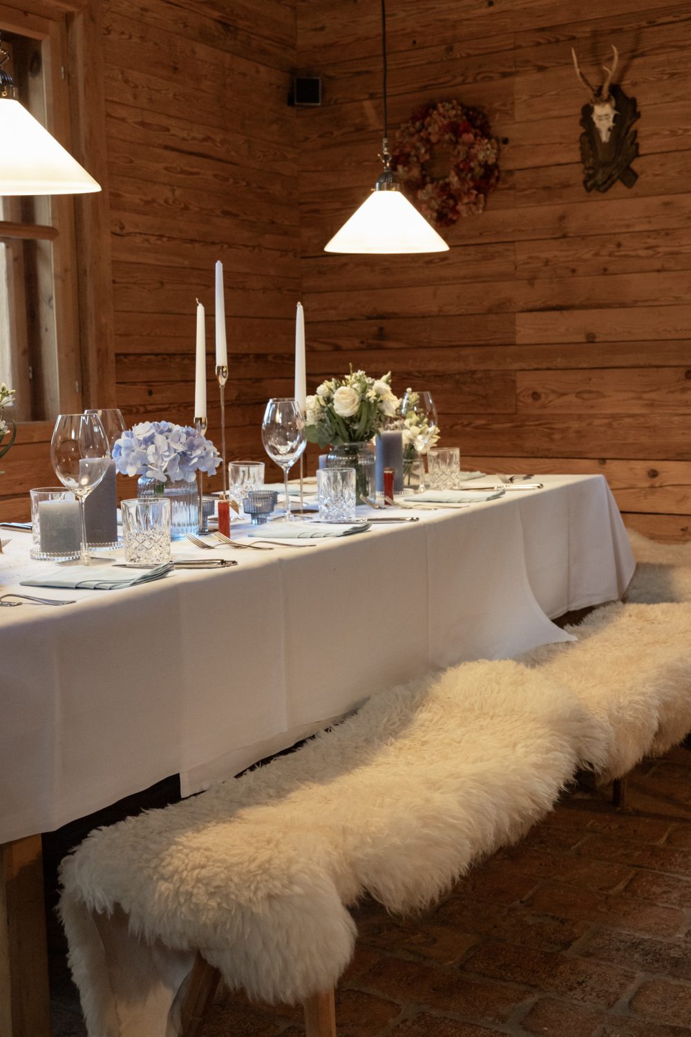 Lange gedeckte Tafel in einer Holzstube, davor eine Bank mit Fell