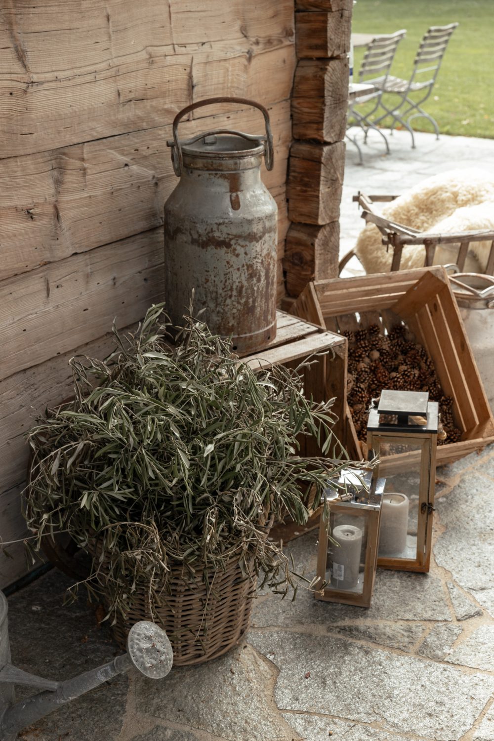 Milchkanne, Korb mit Holz, Pflanze und Laternen an einer Holzwand