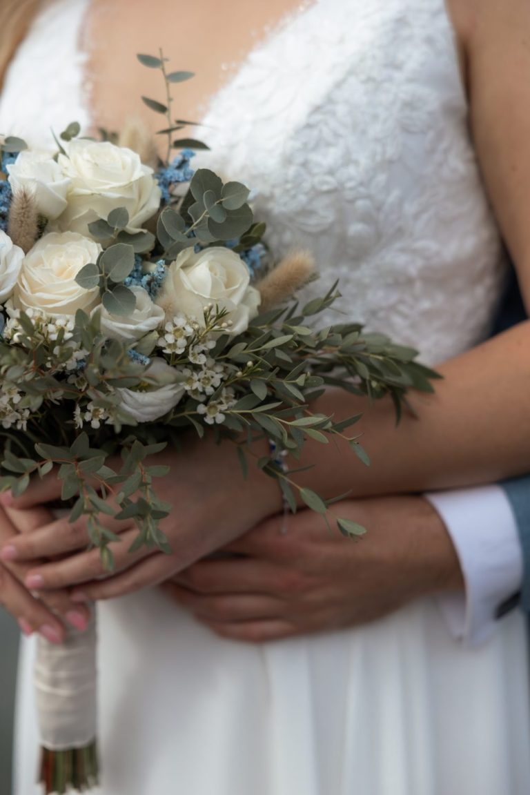 Braut hält einen Brautstrauß mit weißen Rosen und blauen Blüten