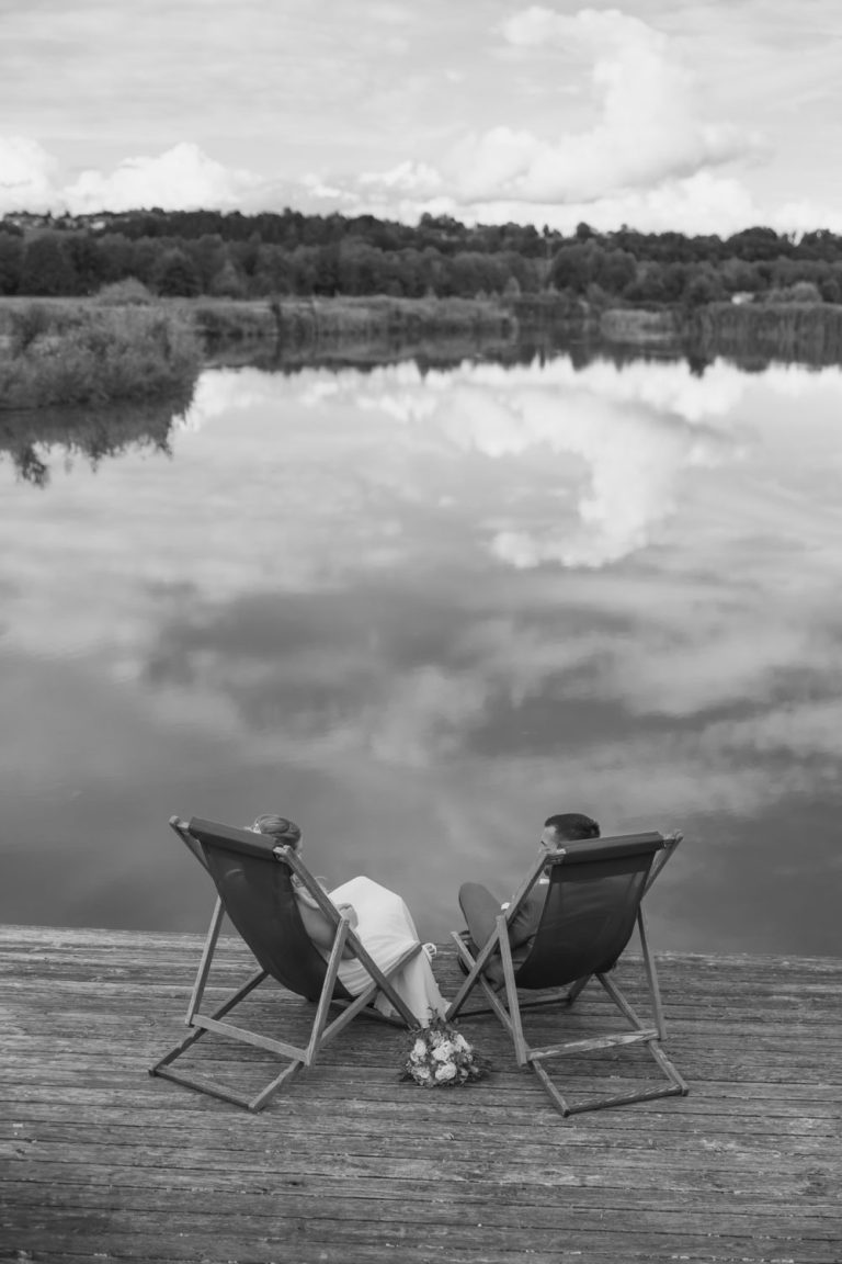 Zwei Liegestühle auf einem Steg am See (Schwarz-Weiß-Aufnahme)